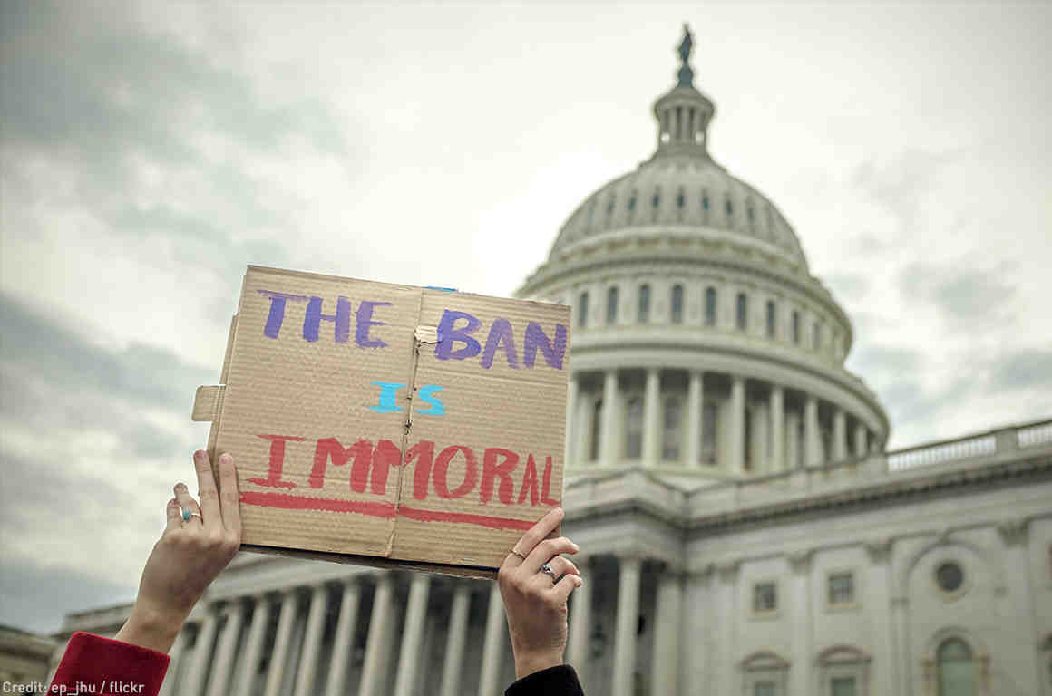 Person holding "The Ban Is Immoral" sign in front of Capitol building