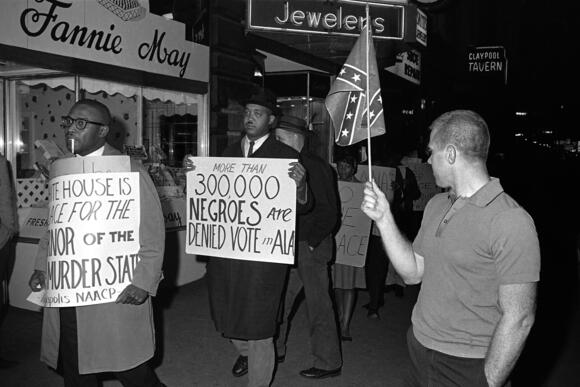 Man holding a Confederate flag at right and a demonstrator carrying a sign with the text: &quot;More than 300,000 Negroes are Denied Vote in Ala&quot;