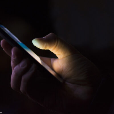 A hand holding a smart phone shrouded in darkness.