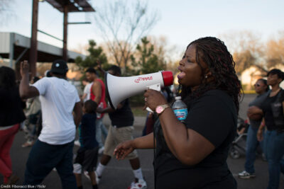 A Black woman using a megaphone at a daytime Black Lives Matter march in Minneapolis, Minnesota in response to police shooting of 18-year-old Tania Harris.