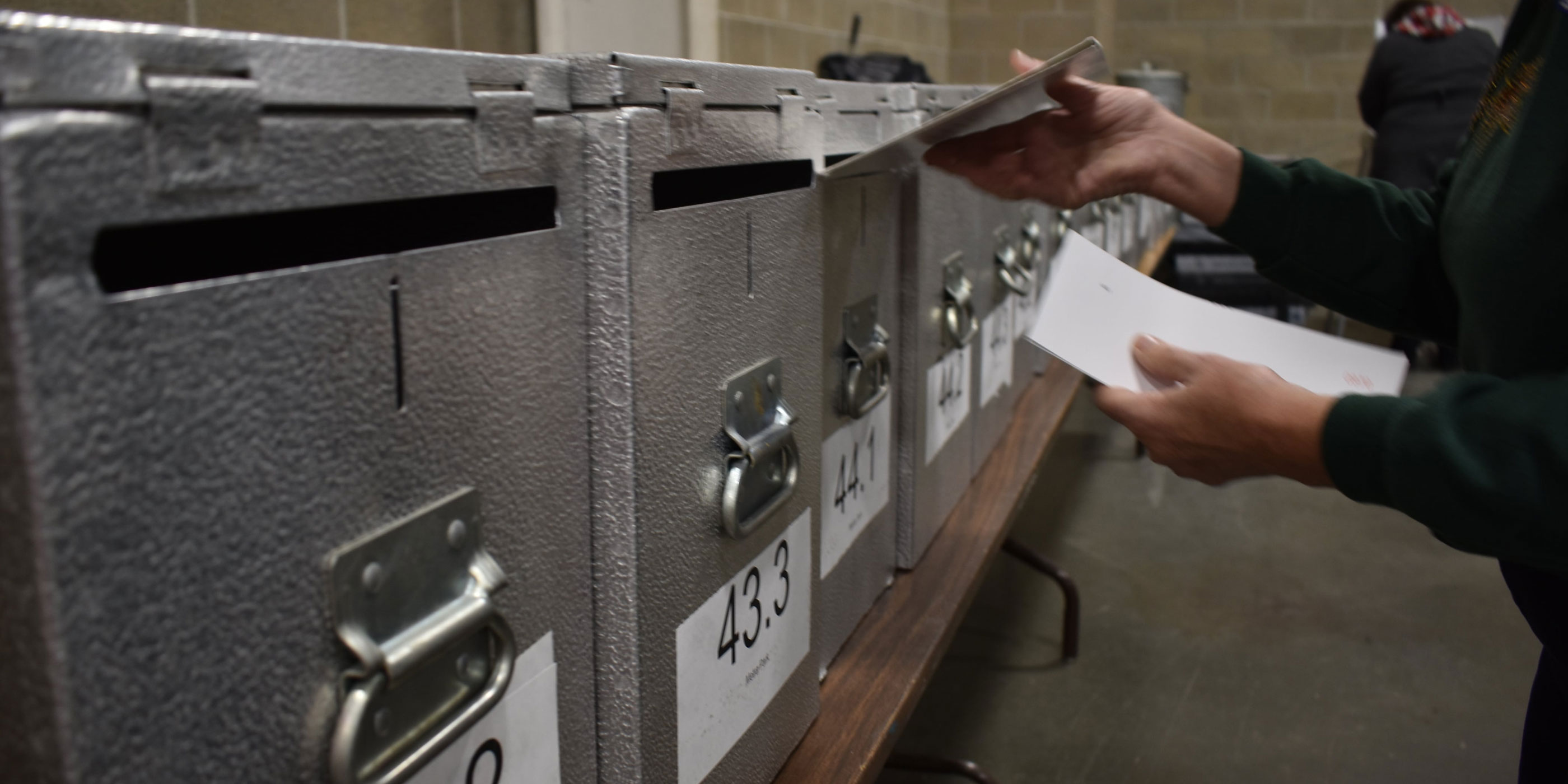 An election worker inserting a ballot into a locked ballot box.