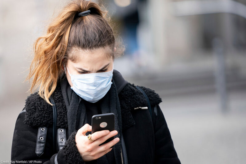 A woman wearing a mask looks at her smartphone.