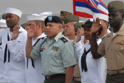 Sailors and Marines with right hands raised taking the oath of citizenship aboard the USS Cleveland.