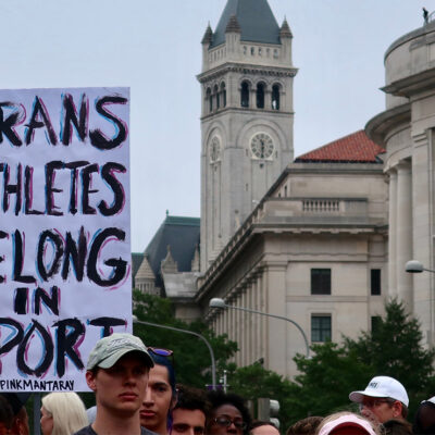 A crowd of marchers with one holding a sign with the text " Trans Athletes Belong in Sport."