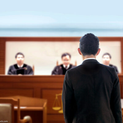 Back of lawyer talking to judges in a courtroom.