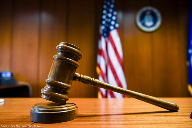 A gavel rests on the judge’s bench in a courtroom with American flag in the background.