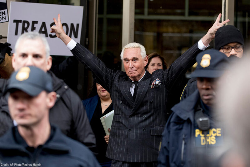 Roger Stone leaving federal court with raised arms wide and flashing two V-shaped hand signs.