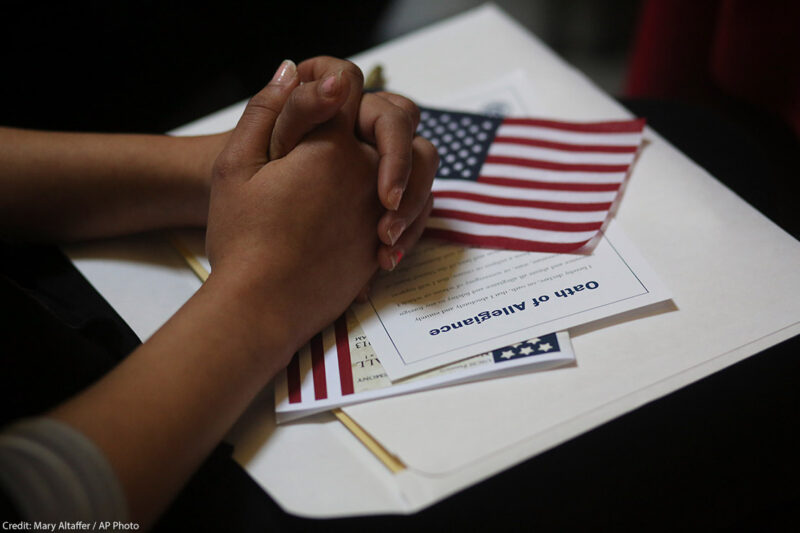 A participant folds her hands of a copy of the Oath of Allegiance and an American flag while listening to speeches during a naturalization ceremony