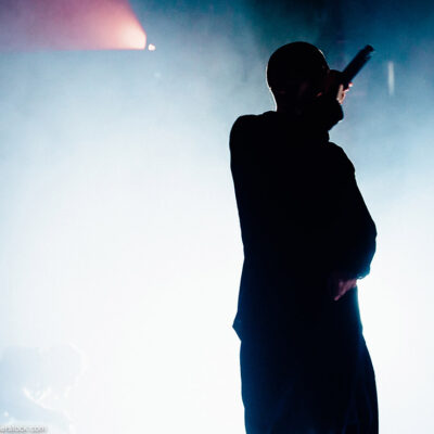 Silhouette of a rapper onstage with bright stage light and smoke in the background.