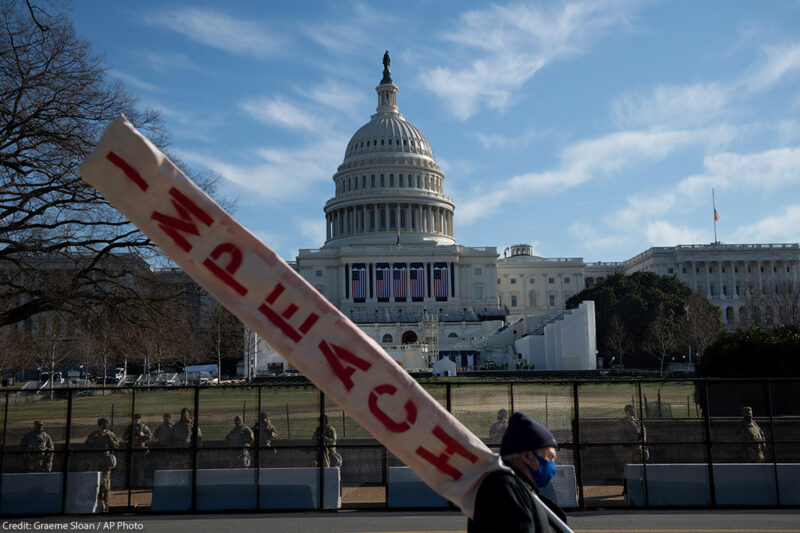A man walks by the U.S. Capitol Building carrying a sign that reads "Impeach"
