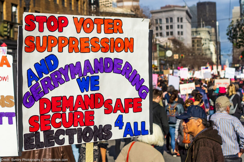 A demonstrator carries a sign demanding an end to gerrymandering and voter suppression.