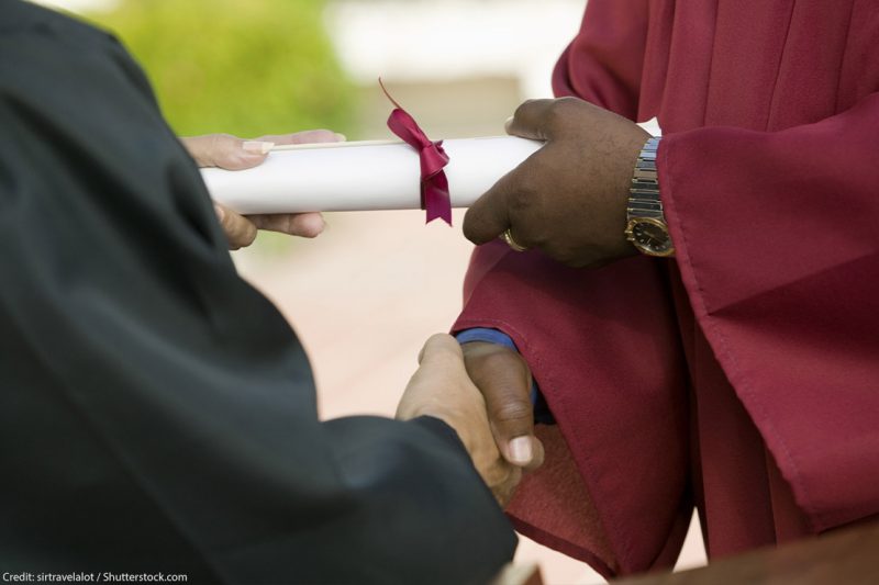 A black man receiving his diploma and giving a handshake.