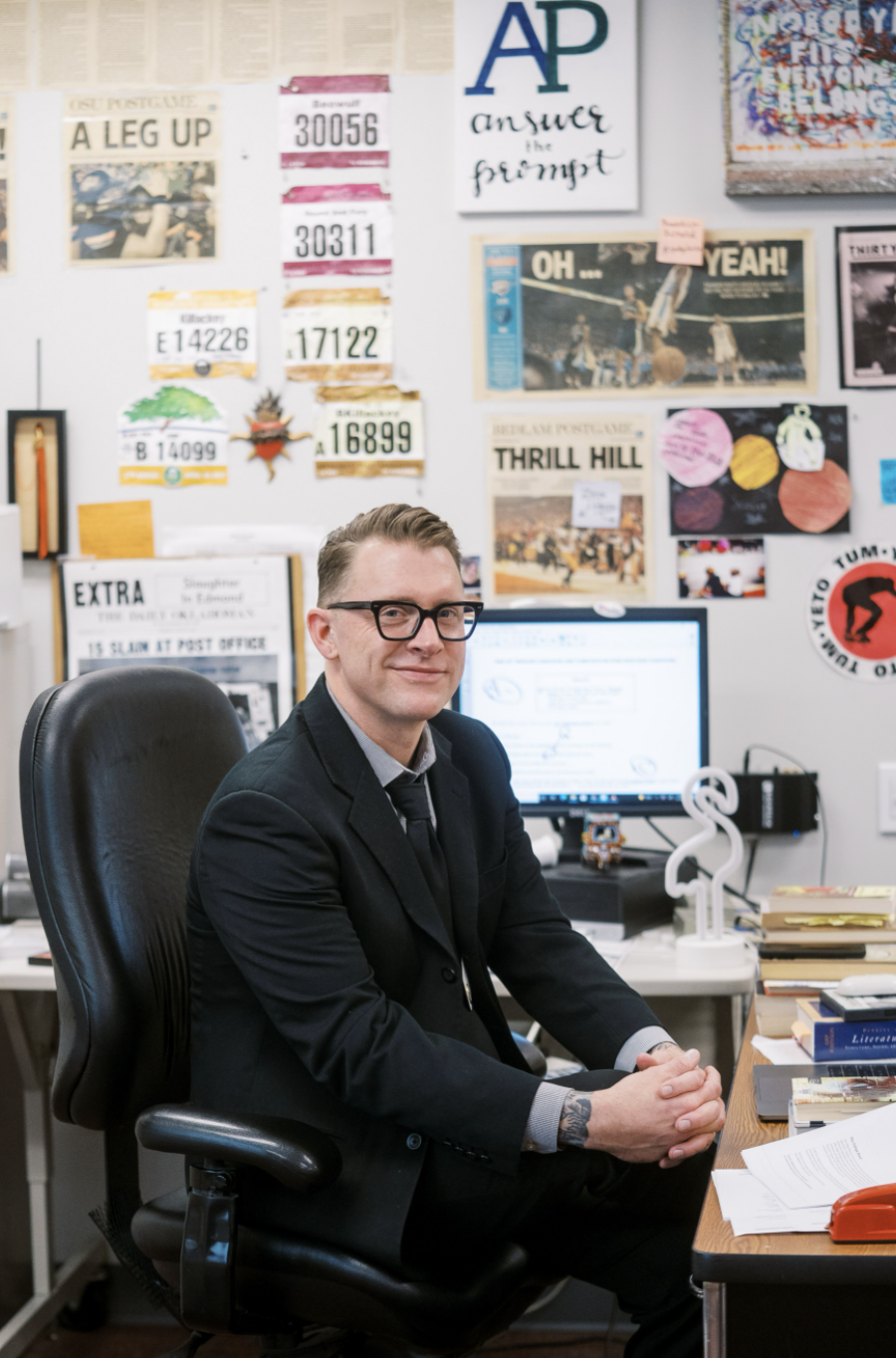 Regan sits at his office desk with laptop and wall art behind him