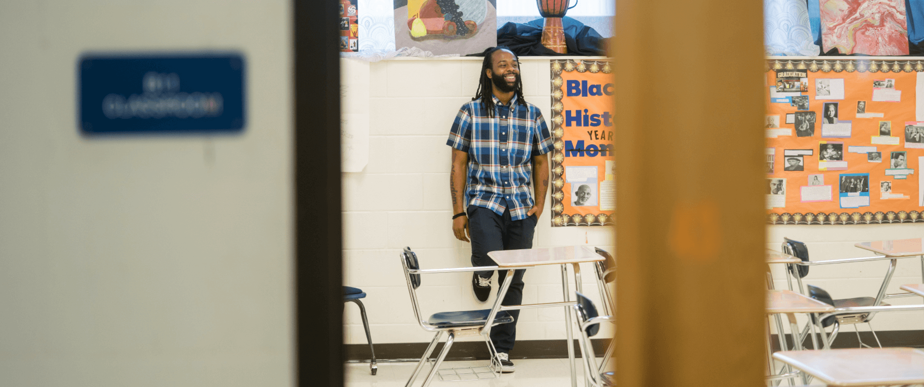 Door is creaked open as Anthony stands in his classroom with one foot up against wall.