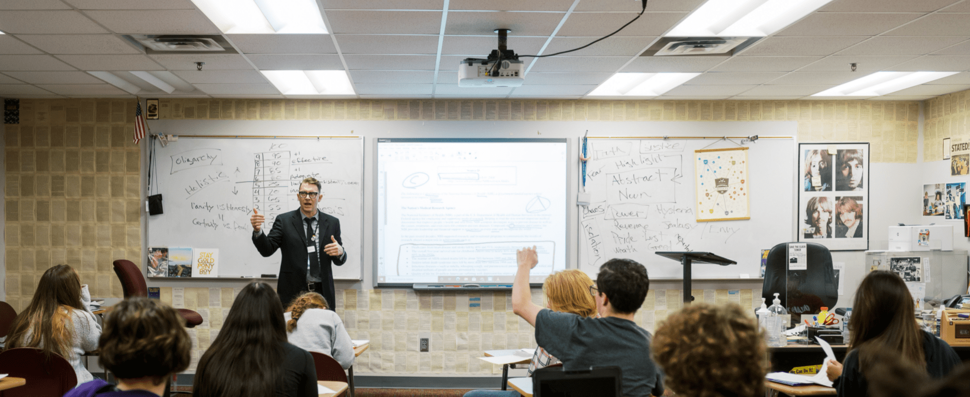 Regan is teaching about oligarchy in the front of his classroom as students raise hands