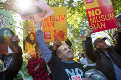 Demonstrators holding signs, one of which says “No Muslim Ban.”