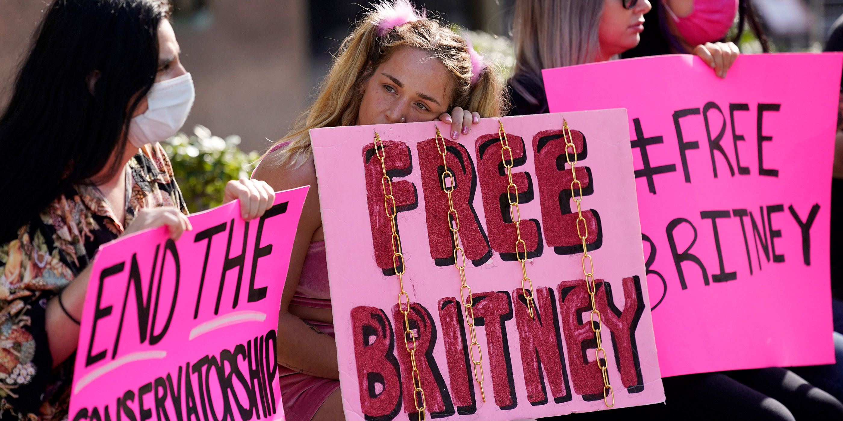 Britney Spears supporters sit outside a court hearing holding signs reading “End The Conservatorship,” and “Free Britney.”