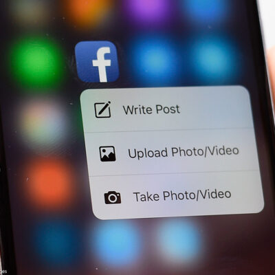 A hand holding a phone with a Facebook app on the screen.