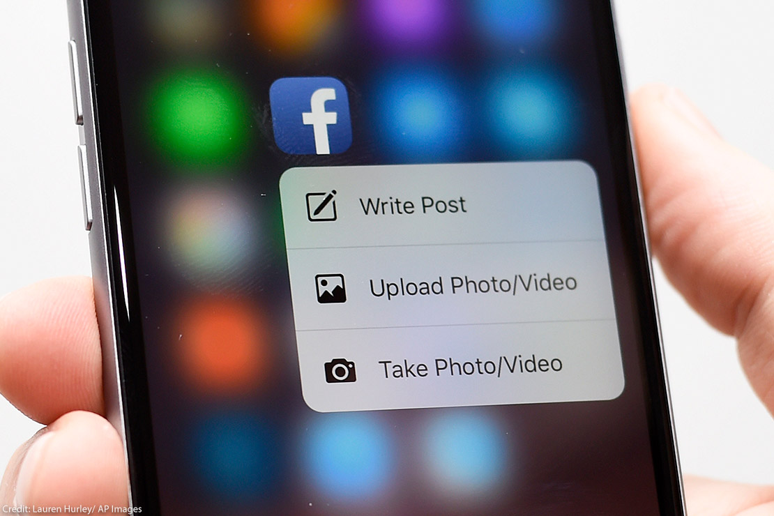 A hand holding a phone with a Facebook app on the screen.