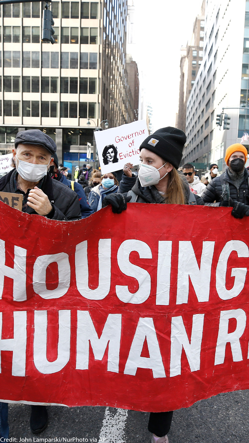 Protesters marching and holding a sign reading Housing Is A Human Right.