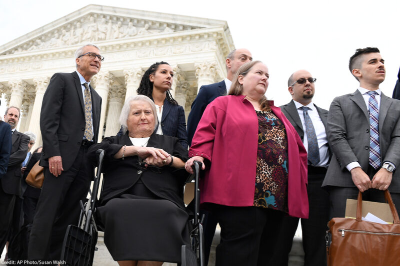 Aimee Stephens, seated, her wife Donna Stephens, in pink, and ACLU attorney Chase Strangio, at the far right listen during a news conference outside the Supreme Court.