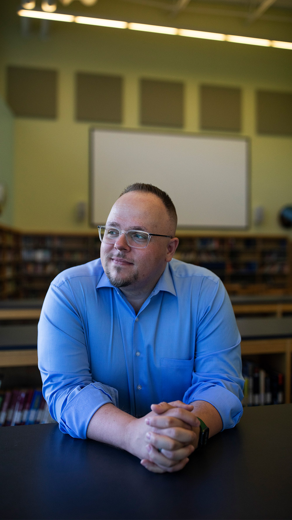 Jared McGarvey leaning forward on a bookcase with his hands folded.