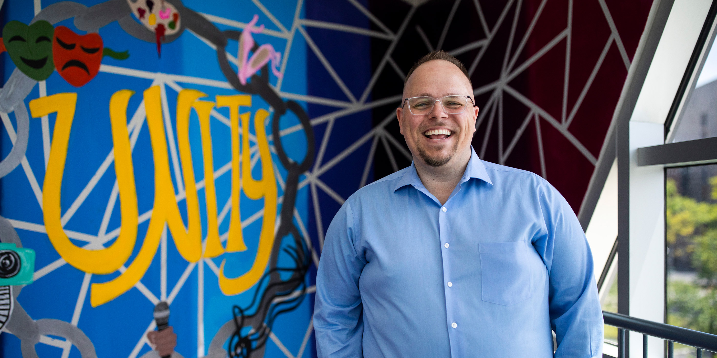 A smiling Jared McGarvey standing next to a mural with the word Unity.