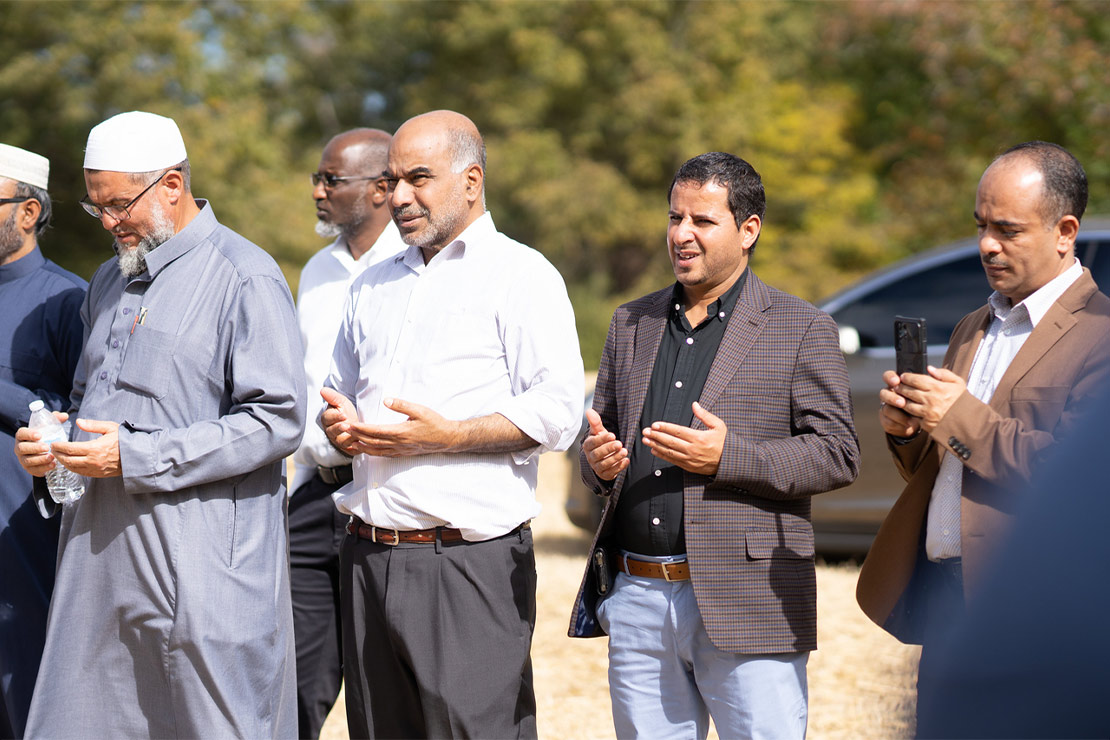 Three middle-aged men (members of the Abraham House of God, the first mosque in DeSoto County Mississippi) pray with palms facing up while another captures the event on his cellphone.