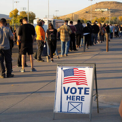 A sign that says "vote here" among a line of voters.