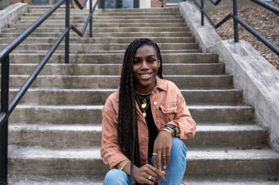 Photo of Andraya Yearwood, a Black woman, sitting at the bottom of grey concrete steps.