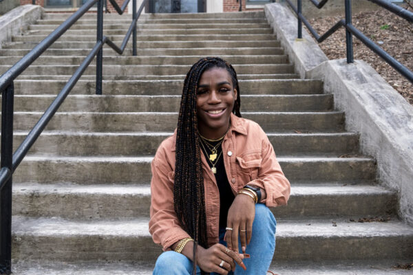 Photo of Andraya Yearwood, a Black woman, sitting at the bottom of grey concrete steps.