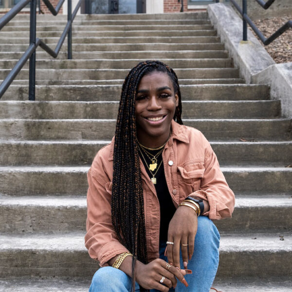 Photo of Andraya Yearwood, a Black woman, sitting at the bottom of grey concrete steps.
