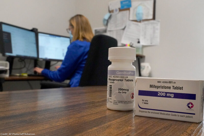 A box of the drug mifepristone pictured in front of a women on a computer.