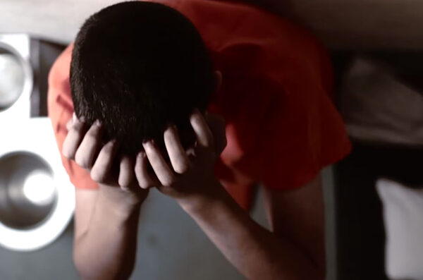 Young prisoner in juvenile solitary with head between hands