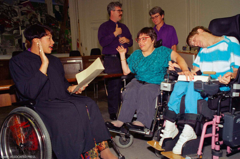 Judy Heumann, center wheelchair, is sworn in as U.S. Assistant Secretary for Special Education and Rehabilitative Service by Judge Gail Bereola, left, on June 29, 1993. Standing at left is Berkeley Mayor Loni Hancock with sign language interpreter Joseph Quinn, and Julie Weissman, right.