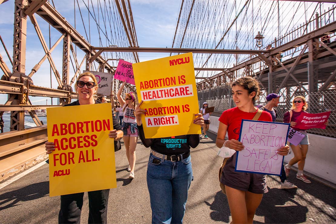 ACLU supporters crossing the Brooklyn Bridge, holding signs reading Abortion Access for All.