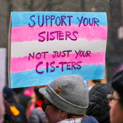 A demonstration sign reading "Support Your Sisters, Not Just Your Cis-ters."