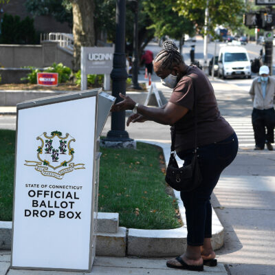 An Afrian-American woman drops a ballot into a State of Connecticut Official Ballot Drop Box outside Hartford City Hall.