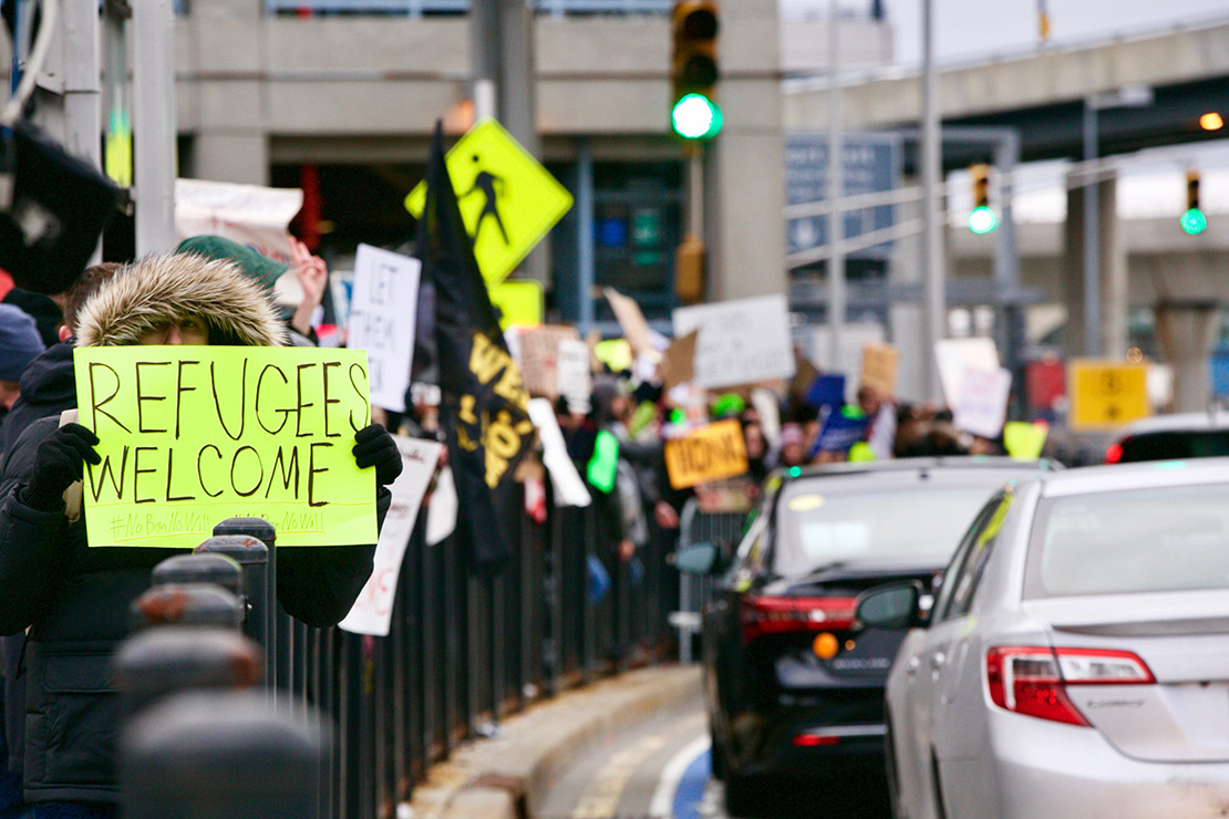 A demonstrator holds a sign near a road that says "Refugees Welcome."