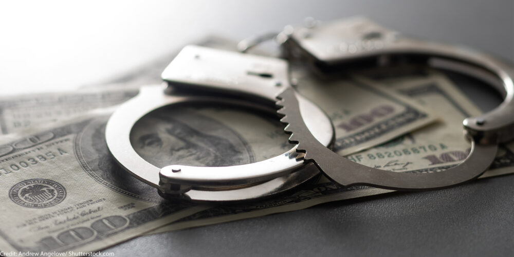 A pair of handcuffs on top of several hundred dollar bills.