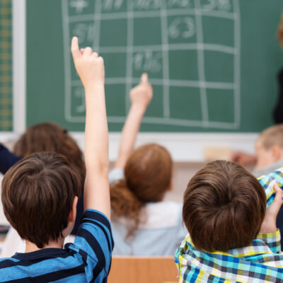 Middle school students raising hands to answer teacher.