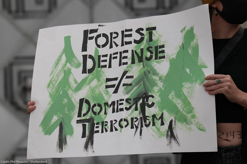 A protester holdng a sign stating "Forest Defense =/ Domestic Terrorism" demands the end of planned construction of Atlanta's proposed police training facility, "Cop City" to save the Weelaunee Forest.