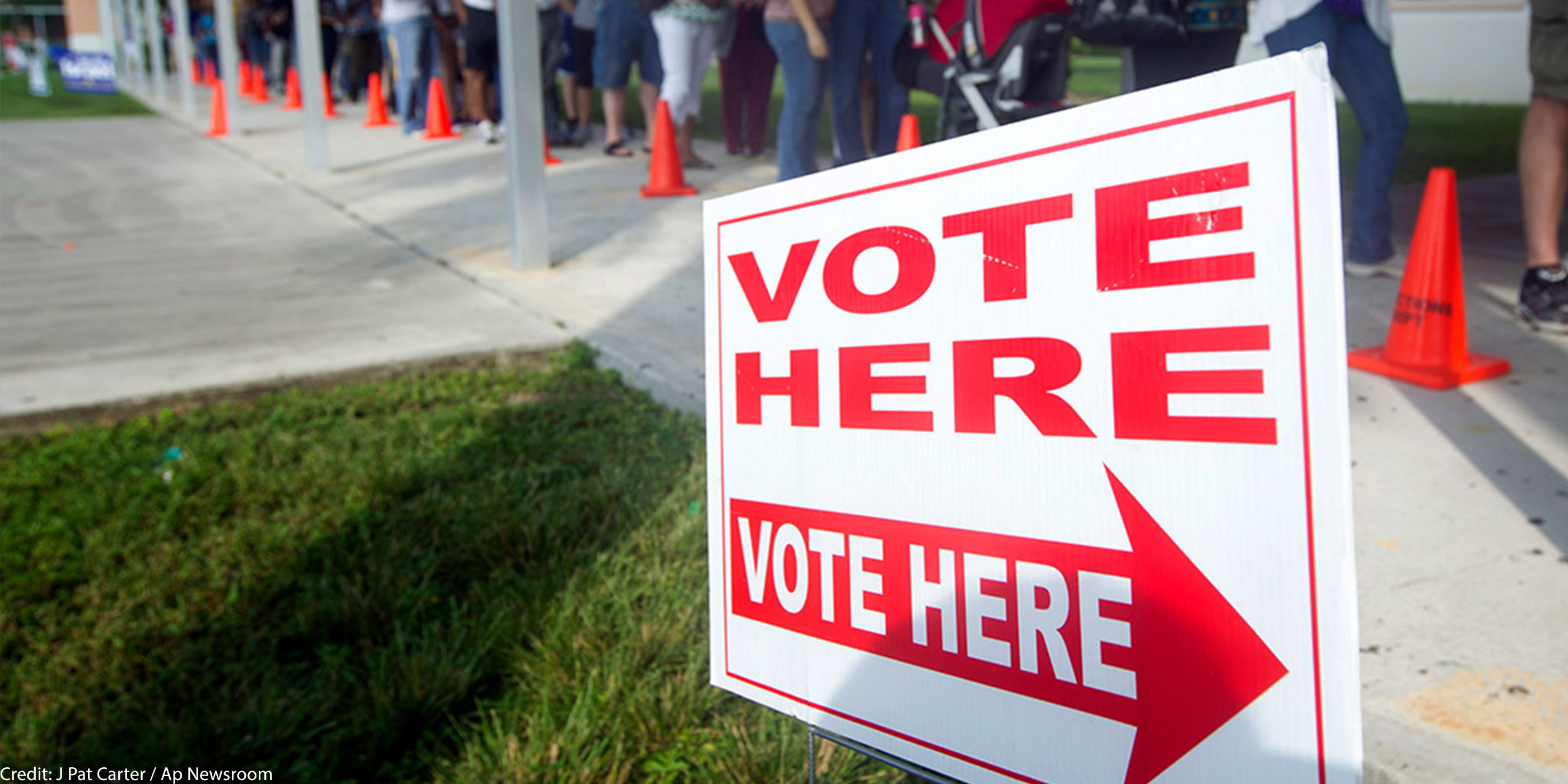 A line of voters in front of a sign that says "vote here."