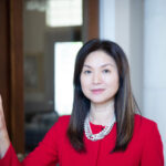 Headshot of attorney Echo King with a closed-mouth smile, She is standing in front of a building with a glass door, and wearing a red cardigan and pearl necklace.