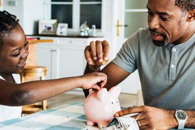 Black father and daughter saving money to piggy bank