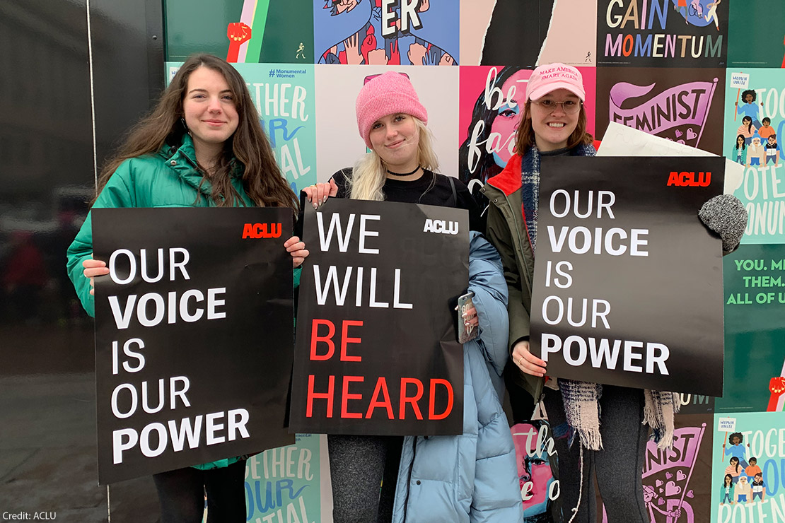 Three individuals holding ACLU branded posters.