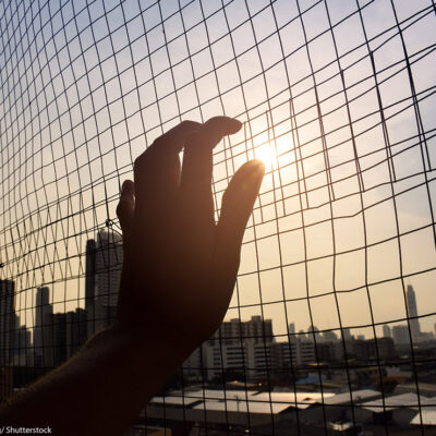 The silhouette of a hand holding on to a gate.
