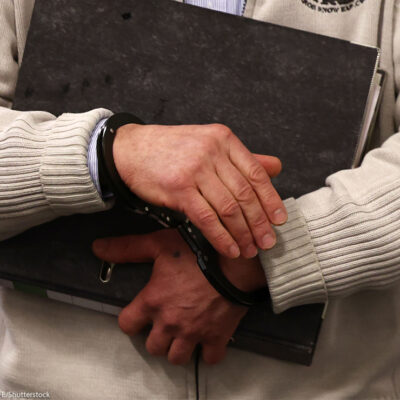 Person holding binder and is in handcuffs.